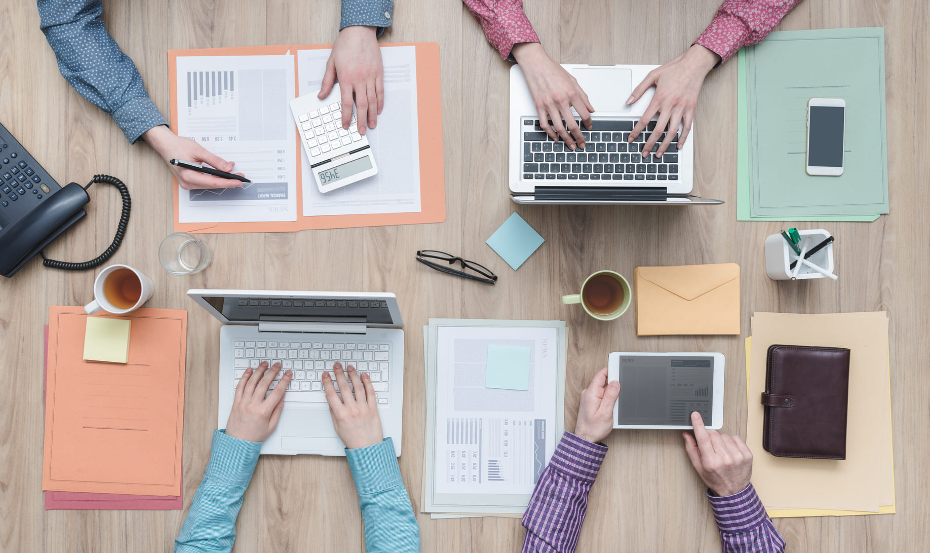 Cuatro personas trabajando juntas en una mesa con varios dispositivos y documentos.