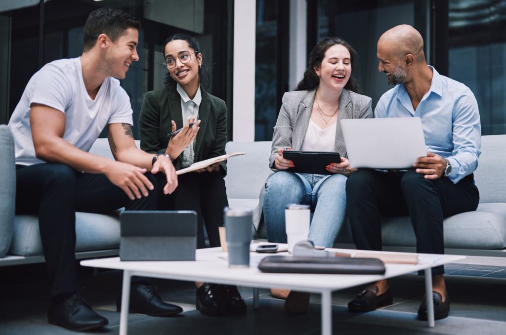 Cuatro profesionales sonrientes en una sesión de trabajo colaborativo con dispositivos electrónicos y notas.