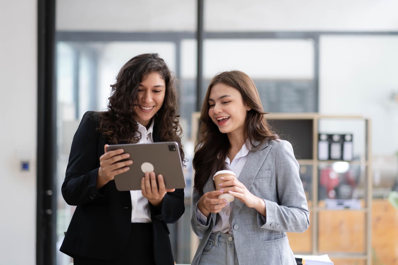 Dos empresarias felices revisando contenido en una tableta en una oficina moderna.