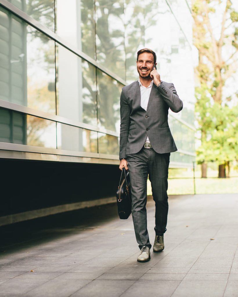 Hombre de negocios sonriente caminando al aire libre con un maletín, hablando por teléfono.