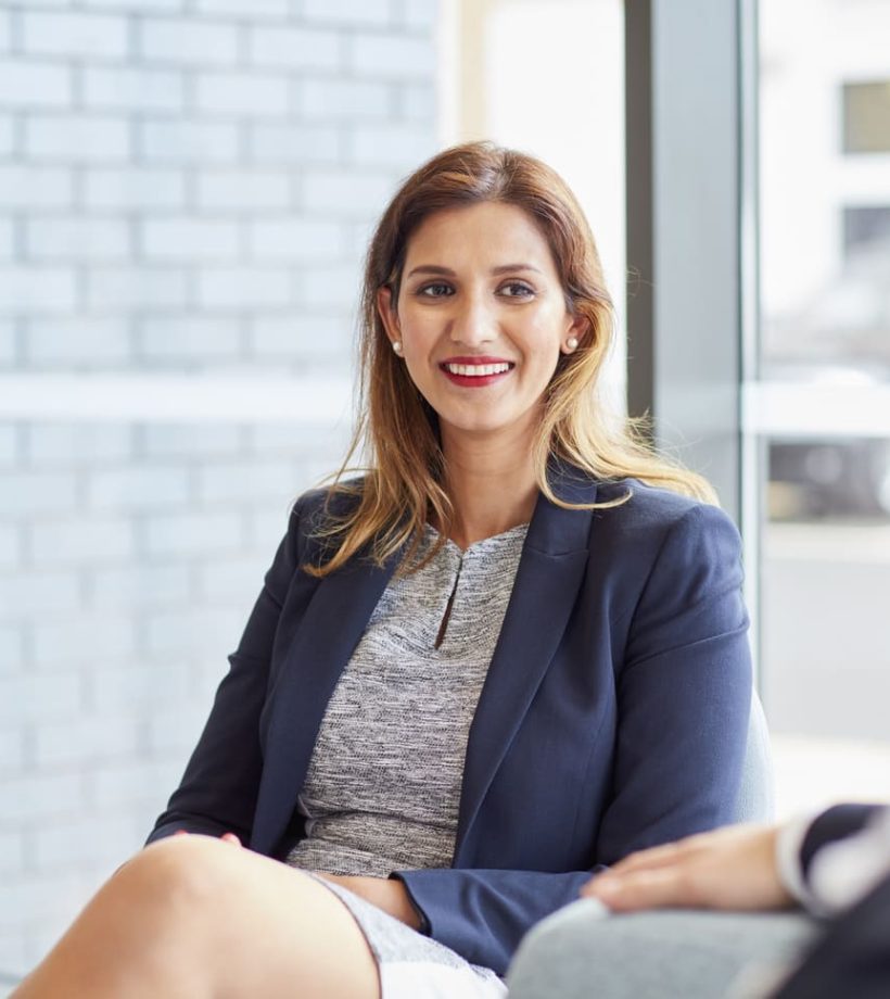 Una empresaria sonriente sentada en una sala de reuniones conversando con un colega.